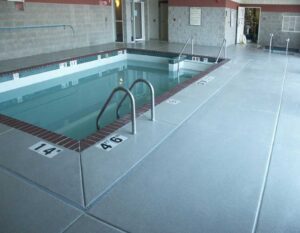 Decorative Floor Coatings for Pool Areas featuring a smooth, slip-resistant surface surrounding an indoor pool with depth markers and safety railings.