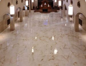 Decorate Marble Floor Coatings in a large, elegant interior space with a high-gloss white and gold marbled finish, reflecting soft lighting and architectural arches.