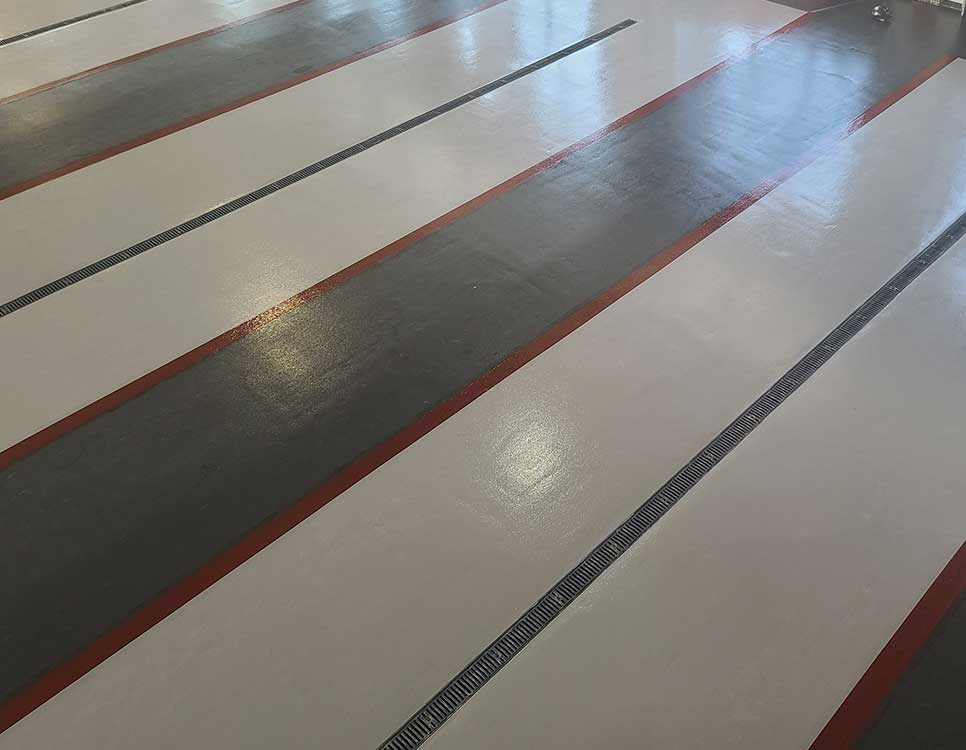 Urethane Cement Flooring Industrial application featuring alternating light and dark coated sections with embedded trench drains for durability and drainage control.