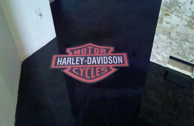 Decorative Floor Coatings Featuring Logo or Designs with a high-gloss black epoxy finish and embedded Harley-Davidson logo in a custom interior space.