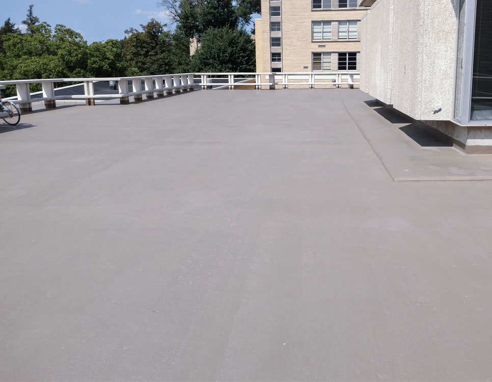 Outdoor Coatings & Sealants applied to a flat rooftop, providing a smooth, protective finish surrounded by railings and adjacent building structures.